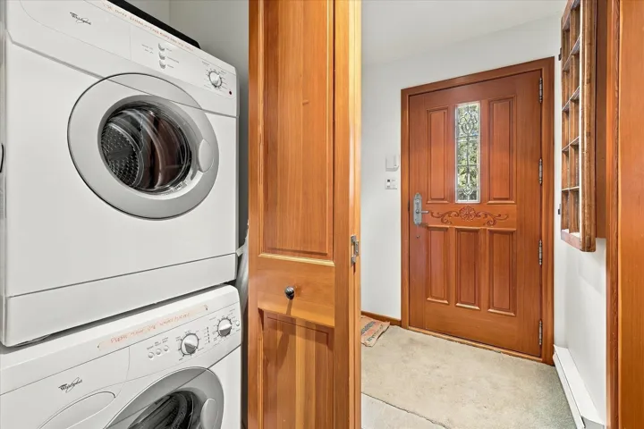 Stacked laundry appliances, wood-paneled door, decorative glass door insert, and light-colored flooring