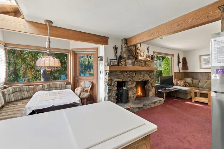 Stone-clad fireplace with a wood mantle, exposed wood beams, wood-frame windows, and a built-in banquette seating area