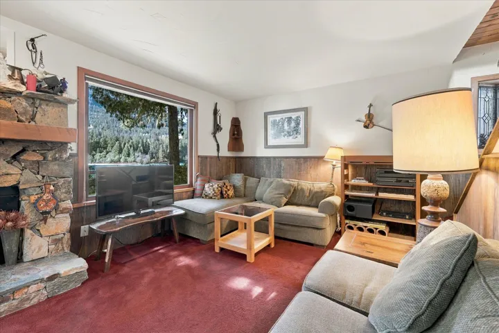 Stone fireplace with a wood mantle, wood-paneled walls, and a large window