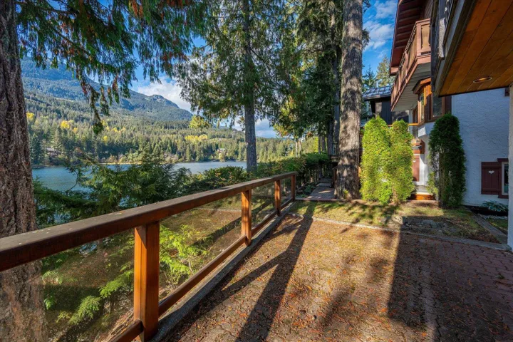 Paved outdoor patio with wood railing, glass panels, and mature trees