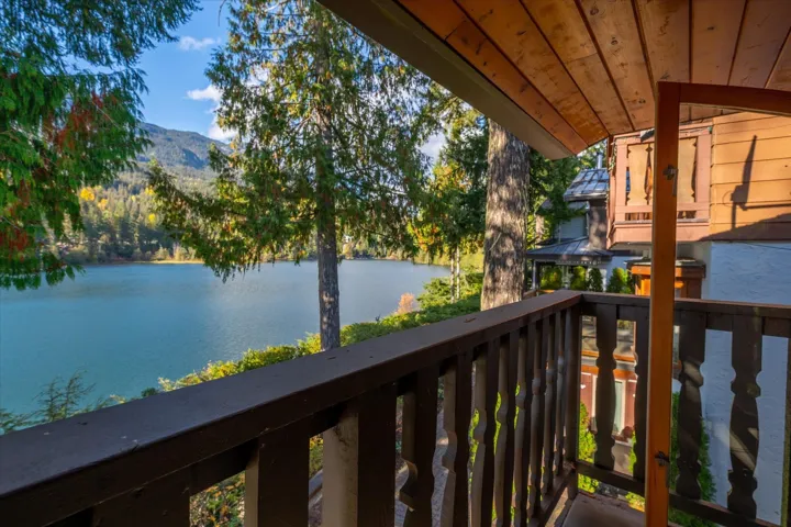 Balcony with wood railing, wood ceiling, and a water backdrop featuring mountains and dense tree coverage