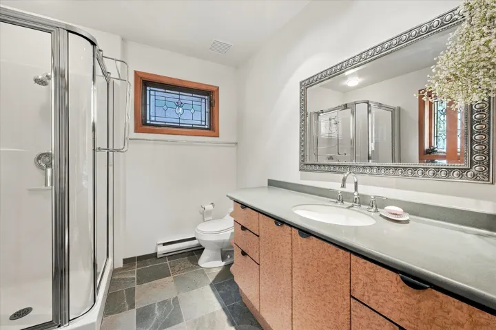 Curved glass shower enclosure, patterned stained glass window, vanity with integrated sink, light-toned countertop, and patterned floor tiling