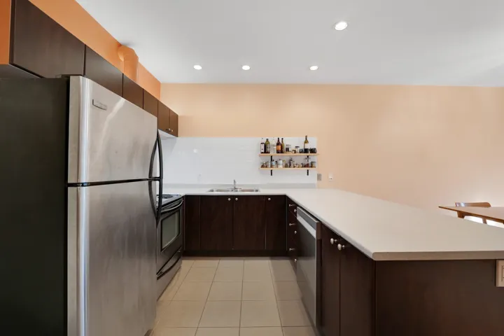 Kitchen featuring stainless steel appliances, dark brown cabinetry, light countertops, a peninsula, and light tile patterned flooring