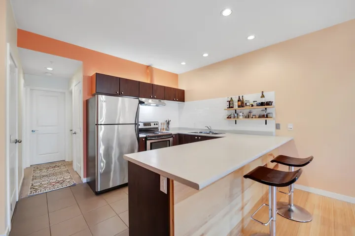 Kitchen with stainless steel appliances, light countertops, a peninsula, dark brown cabinetry, and a kitchen bar