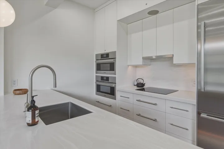 White cabinetry with stainless steel appliances, including stacked ovens and a side-by-side refrigerator