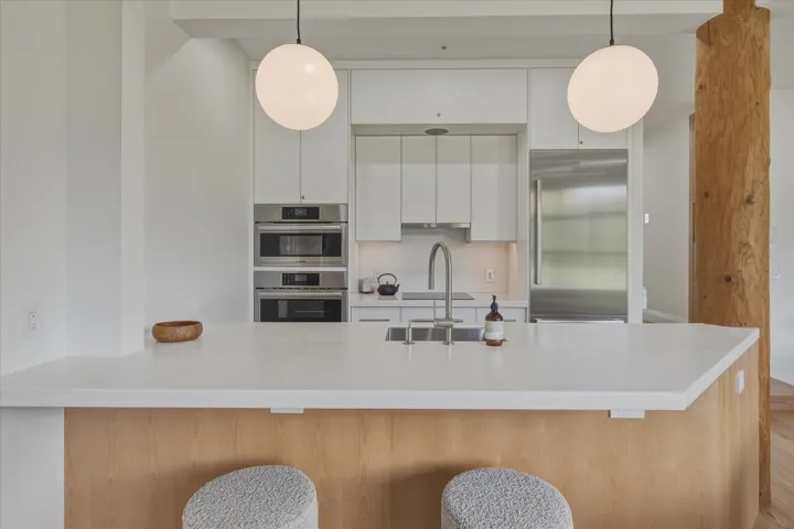 White kitchen cabinetry with integrated stainless steel appliances, a center island featuring a white countertop, and a wood-paneled base