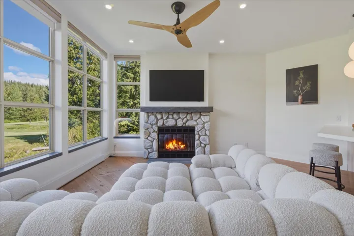 Stone-faced fireplace with a dark mantel, wide-plank wood-finish flooring, and recessed ceiling lighting