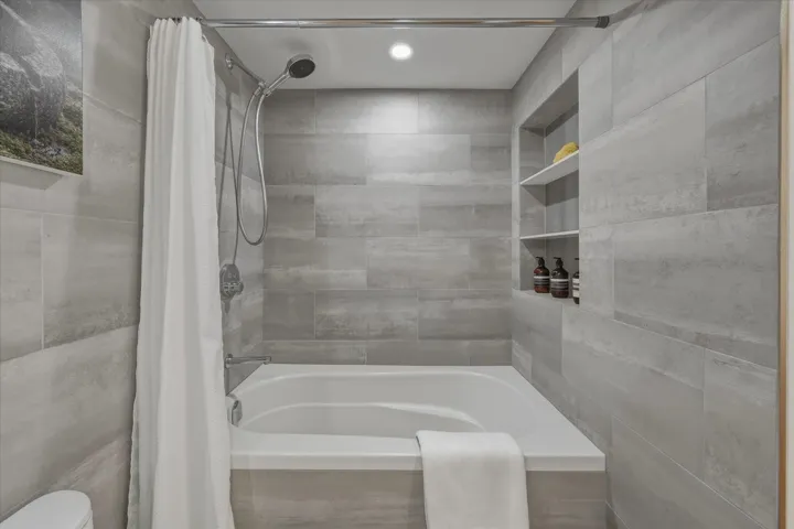 Bathtub with a tiled surround, integrated shower, and recessed shelving