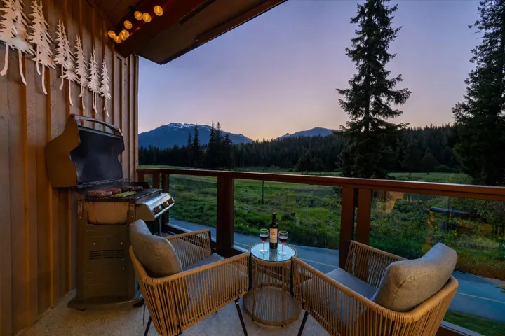 Balcony featuring vertical wood paneling, decorative wall-mounted metal art, and a glass-paneled railing overlooking a forest and distant mountains