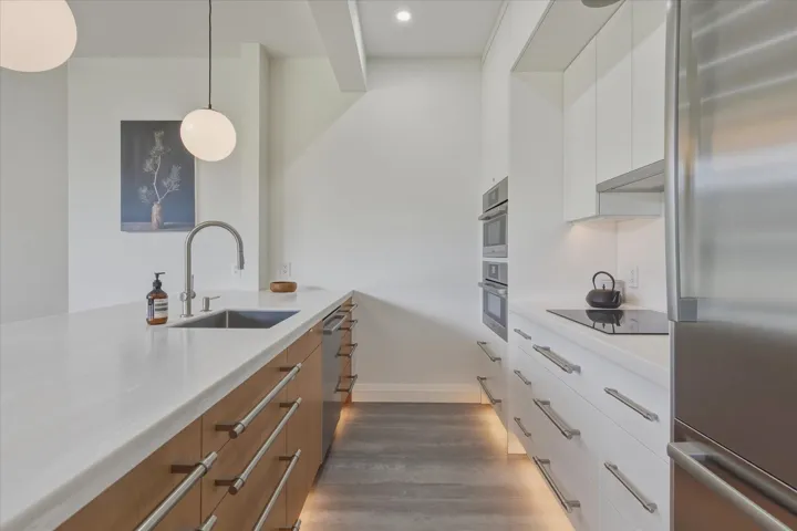 Contemporary kitchen featuring an integrated sink, stainless steel appliances, dual wall ovens, and under-cabinet lighting