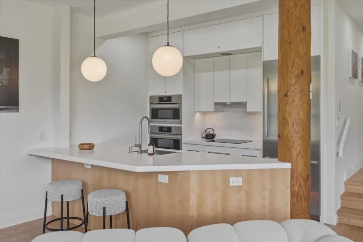 Modern kitchen featuring white cabinetry, integrated stainless steel appliances, a large island with a light-toned countertop, and two spherical pendant lights