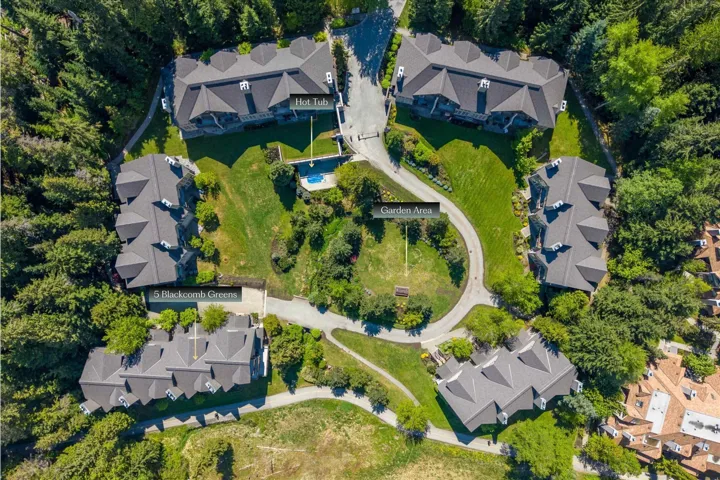 Multiple residences with dark pitched roofs, surrounding a central green space with a garden area and a hot tub