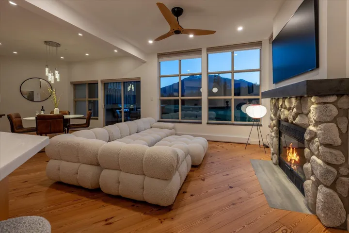 Stone-clad fireplace with concrete mantel, wood-finish flooring, recessed lighting, and large multi-pane windows