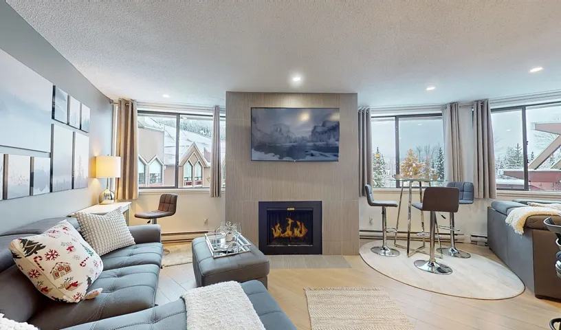Living area with a large fireplace, a textured ceiling, wood-type flooring, a baseboard heating unit, and recessed lighting