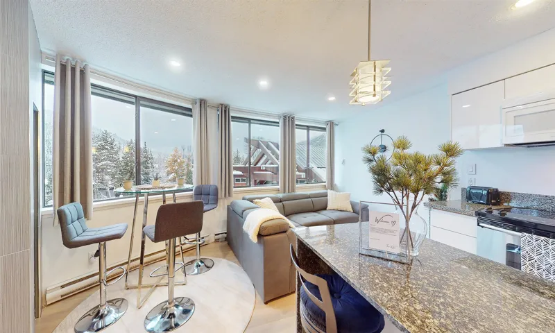 Kitchen with dark stone countertops, decorative light fixtures, a breakfast bar area, light wood-style floors, and white cabinets