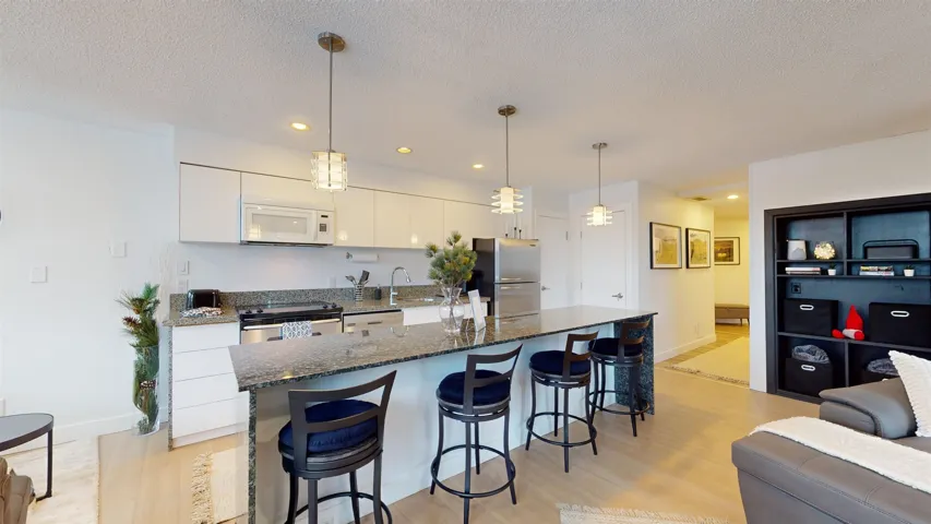 Kitchen with dark stone countertops, decorative light fixtures, a breakfast bar area, light wood-style floors, and white cabinets