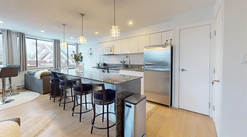 Kitchen with dark stone counters, stainless steel appliances, decorative light fixtures, a kitchen bar, and white cabinetry