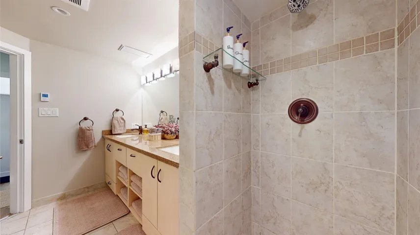 Bathroom with tiled shower, double vanity, and light tile patterned floors
