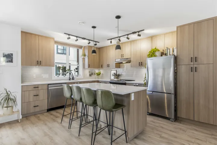 Kitchen featuring wood-finish cabinetry, stainless steel appliances, a center island with countertop seating, white subway tile backsplash, and wood-finish flooring