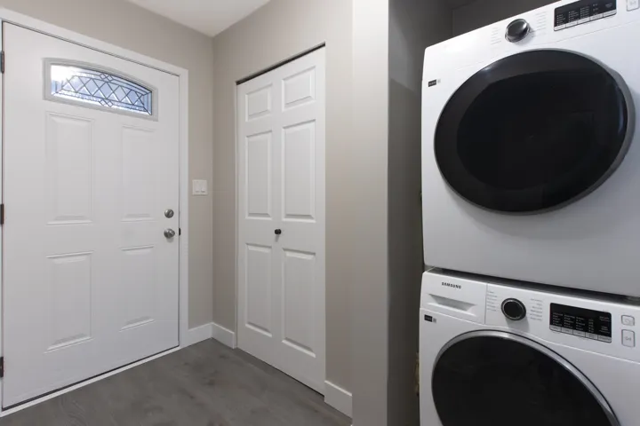 Laundry room with dark wood-style flooring and stacked washer / dryer