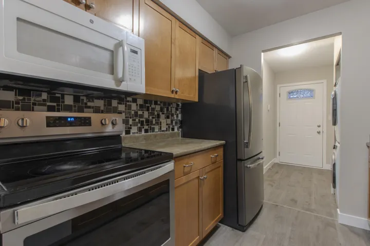 Kitchen featuring appliances with stainless steel finishes, brown cabinetry, backsplash, and stacked washer / dryer