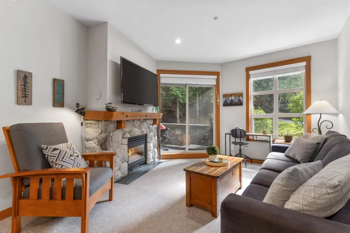 Stone-clad fireplace with a wood mantel, glass sliding doors, and large picture windows with wood trim