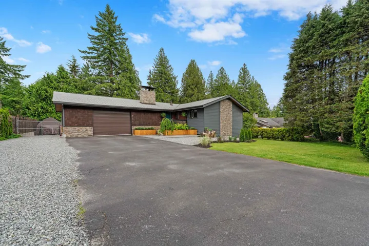 View of front facade with asphalt driveway, a garage, a chimney, stone siding, and a gate