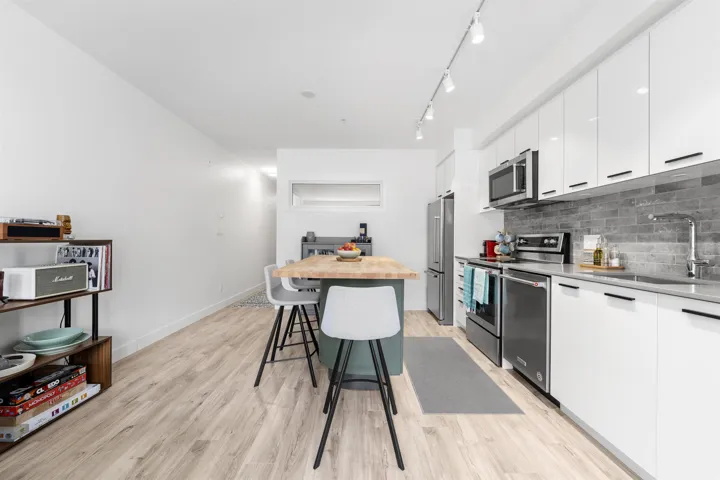 Two tone kitchen featuring stainless steel appliances, light countertops, light wood-style floors, modern cabinets, and a breakfast bar area