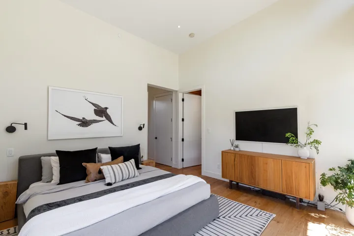 Spacious room featuring vaulted ceilings, wood-finish flooring, two panel doors, and wall-mounted sconces