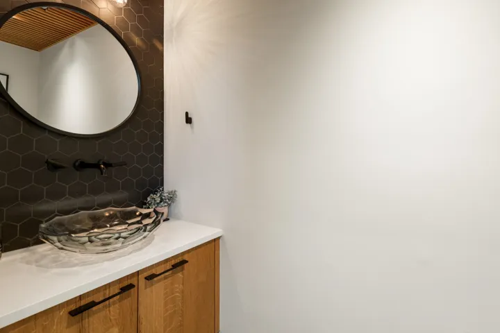 Modern vanity featuring a large vessel sink, wood cabinetry with dark hardware, and a white countertop