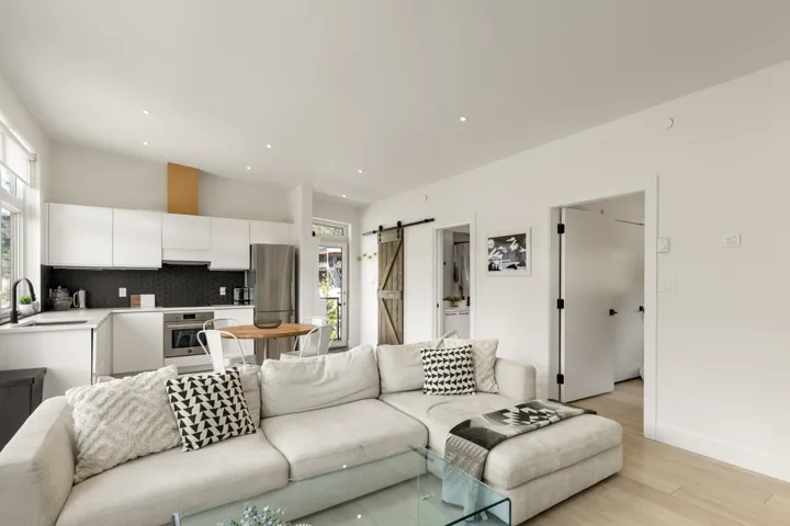Open-concept living area featuring a modern kitchen with white cabinetry, stainless steel appliances, and a dark hexagonal tile backsplash