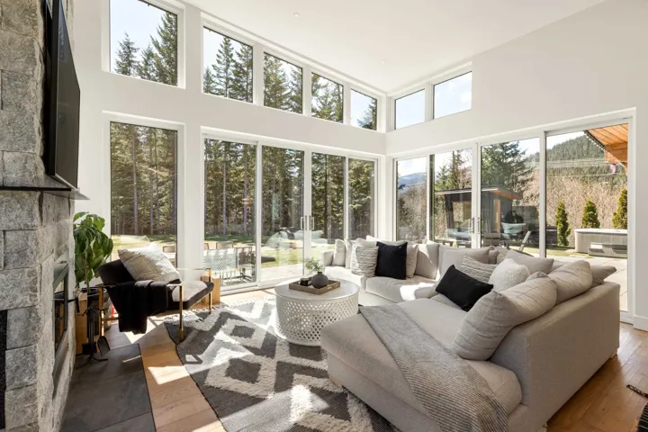 Great room with expansive floor-to-ceiling windows, wood-finish flooring, and a stone-clad fireplace