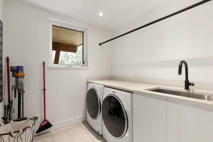 Laundry area featuring a side-by-side washer and dryer, light-toned countertop, integrated stainless steel sink with a matte black faucet, and a black hanging rod