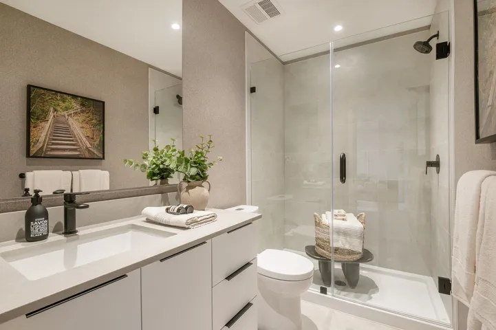 Contemporary bathroom featuring a spacious glass-enclosed shower with matte black fixtures, a single vanity with an integrated rectangular sink, a stone-finish countertop, and white cabinetry with matte black hardware