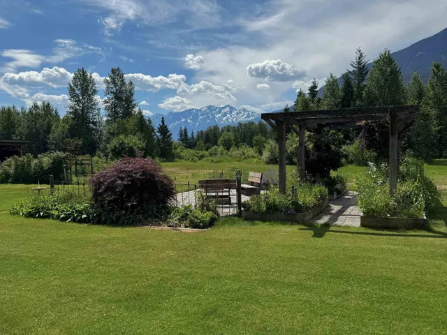 Expansive lawn area featuring a wooden pergola, stone patio, raised garden beds, and mature landscaping