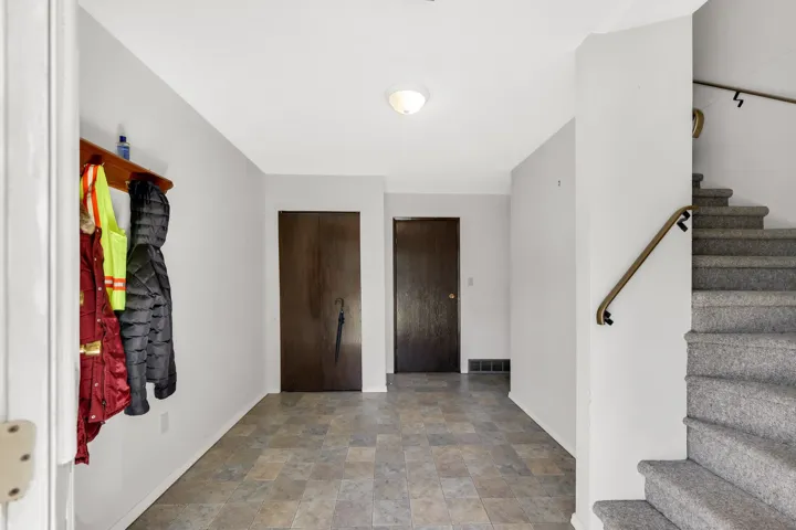 Entryway featuring patterned tile flooring, a built-in coat rack, two dark-paneled doors, and a carpeted staircase with a wood-finish handrail