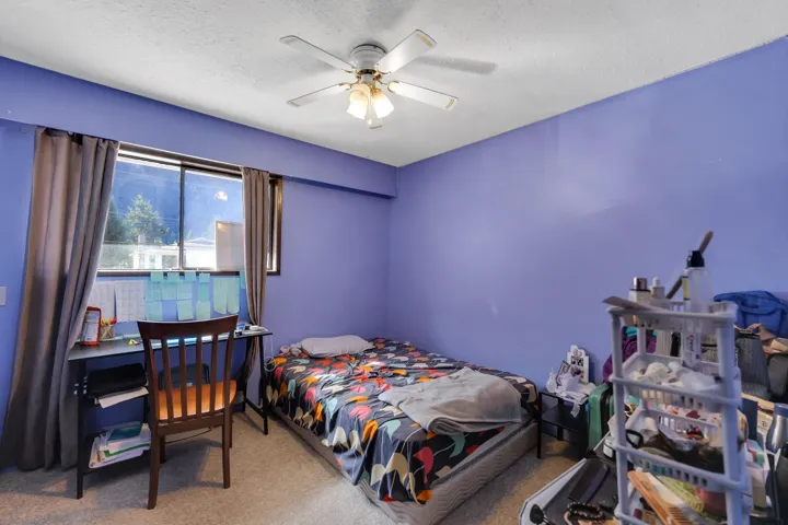 Carpeted room featuring a ceiling fan with integrated lighting, a window with curtains, and a desk area