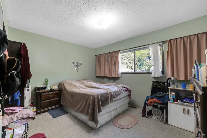 Carpeted bedroom with a window offering natural light, featuring a ceiling-mounted light fixture, light green wall paint, and a dark wood-finish nightstand