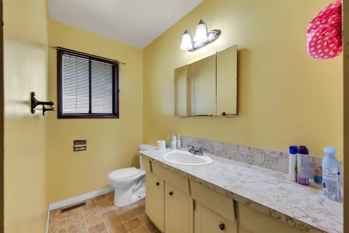 Bathroom featuring a vanity with an integrated sink and patterned countertop, a built-in medicine cabinet, and a window with blinds