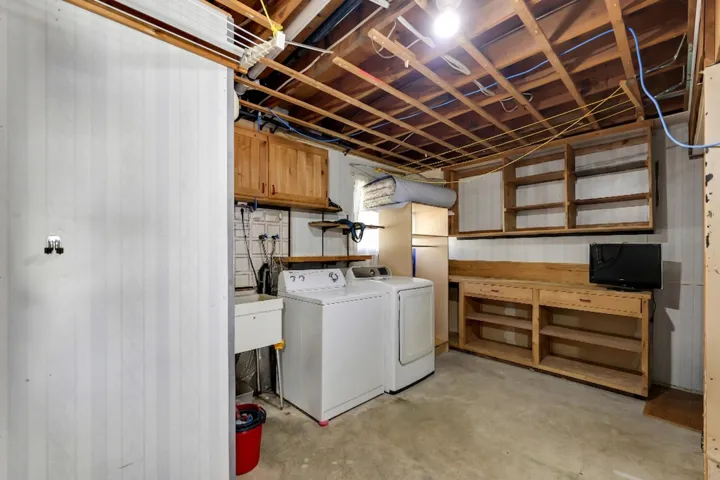 Utility area featuring exposed ceiling joists, concrete flooring, white beadboard wall paneling, built-in wooden shelving, and a utility sink