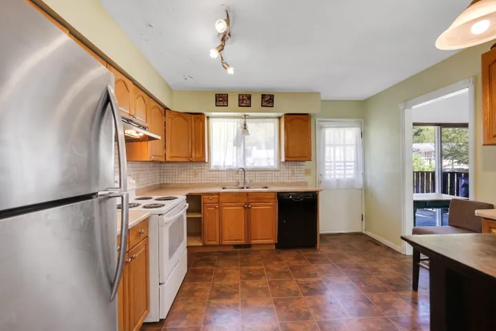 Kitchen featuring wood cabinetry, a stainless steel refrigerator, white range, black dishwasher, and a tiled backsplash