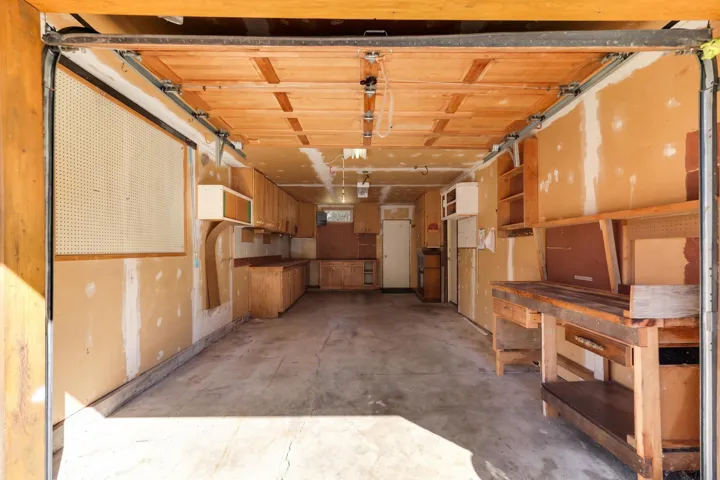 Spacious garage featuring a wood-panel roll-up door, extensive built-in cabinetry, durable concrete flooring, a large workbench, and integrated pegboard storage