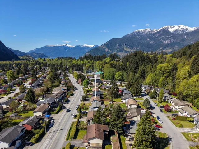 Aerial perspective showcasing a residential area with a prominent road network, bordered by lush green forests and distant snow-capped mountains