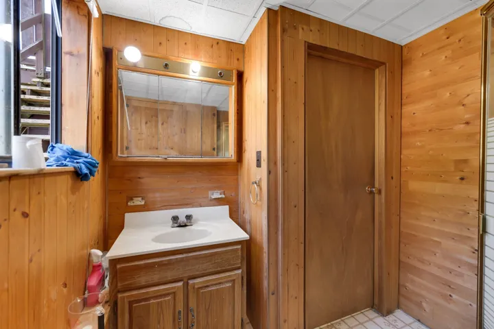 Wood-paneled bathroom with a vanity featuring a white sink and a built-in mirror with integrated lighting