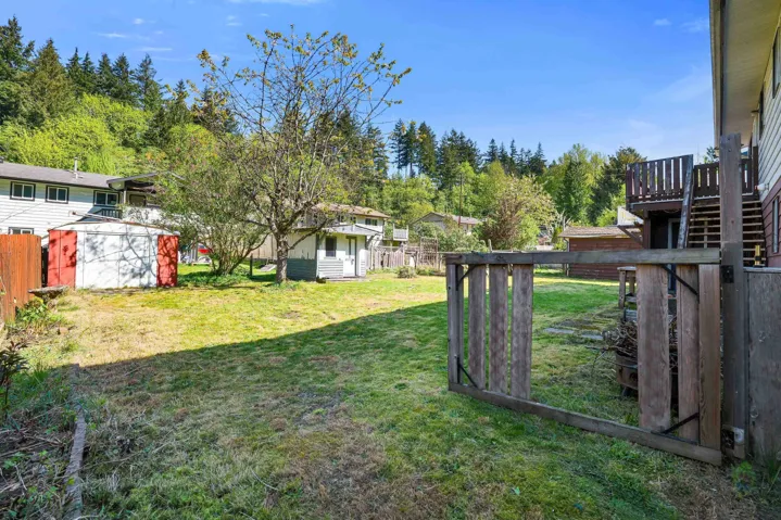Expansive grassy yard area with mature trees, a detached storage shed, and a privacy fence bordering the property
