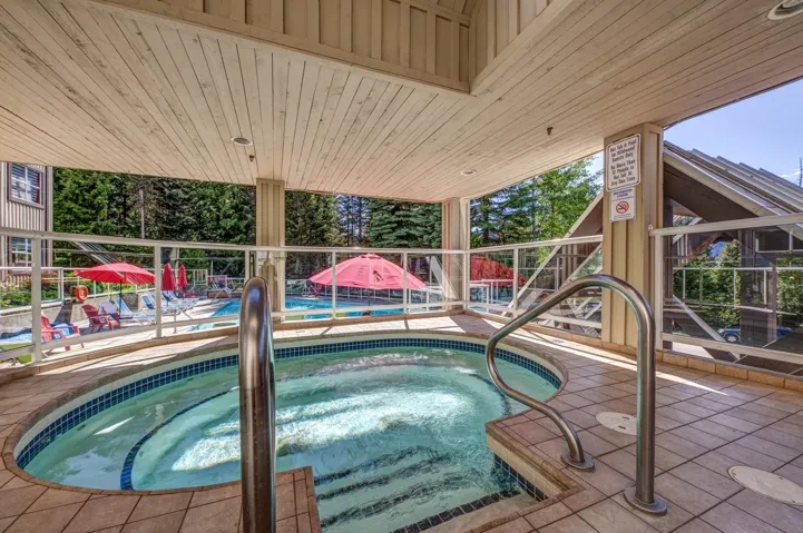 Covered outdoor hot tub featuring a tiled surround, integrated steps, and a stainless steel grab rail