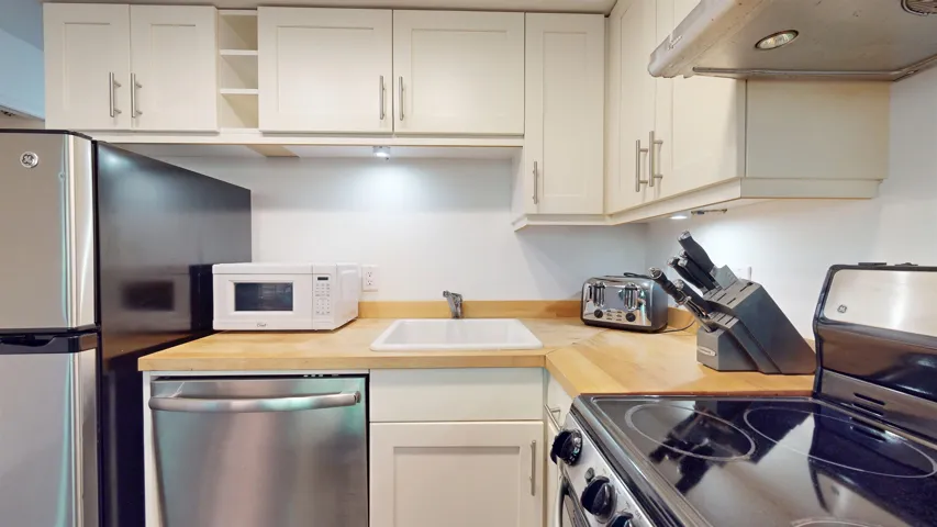 Kitchen with appliances with stainless steel finishes, white cabinetry, extractor fan, open shelves, and wooden counters