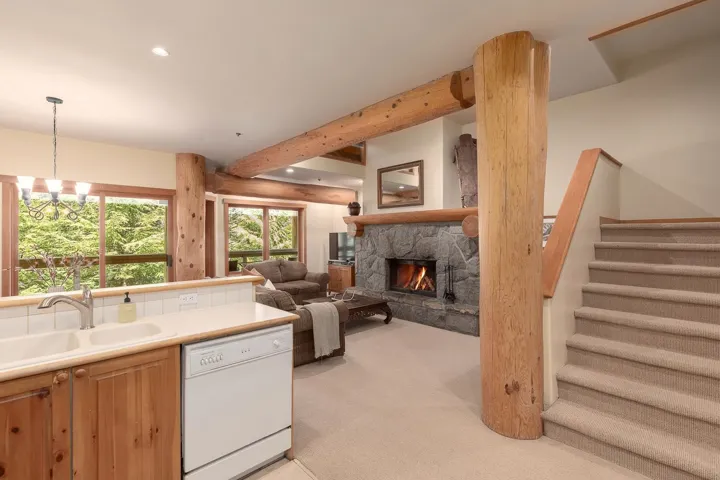Living area featuring a stone fireplace, exposed wood beams, and a carpeted staircase