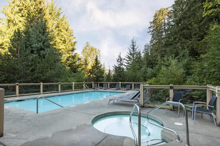 Outdoor swimming pool and spa area with concrete decking and a surrounding glass panel fence