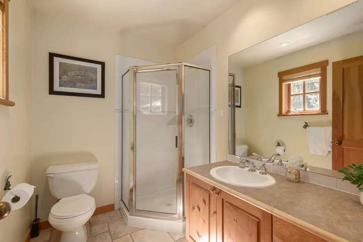 Bathroom featuring a corner glass-enclosed shower, a wood-finish vanity with an integrated sink, a large wall-mounted mirror, a window with wood trim, and neutral-toned wall paint